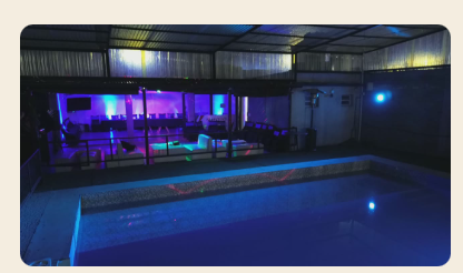 Pileta iluminada de noche con el lounge al fondo